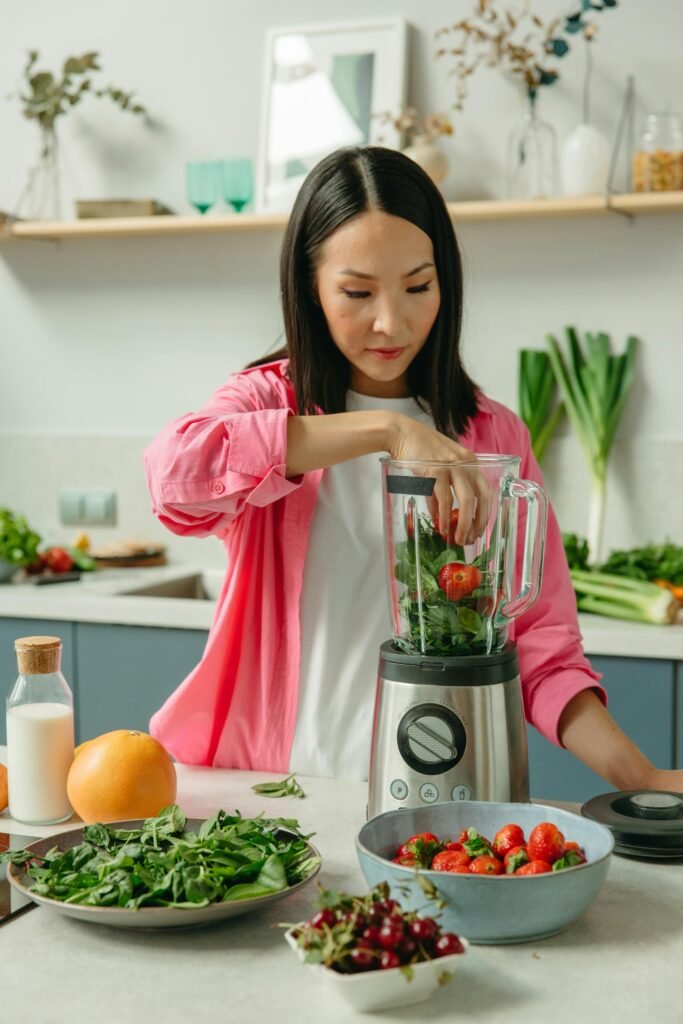 pexels-photo-8845663-8845663 Asian woman making a nutritious green smoothie with fresh vegetables and fruits in a modern kitchen.